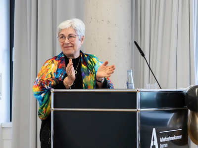 Sybille Böschen steht am Redepult und klatscht in die Hände | © Simone Hryzyk/AWO Bremerhaven